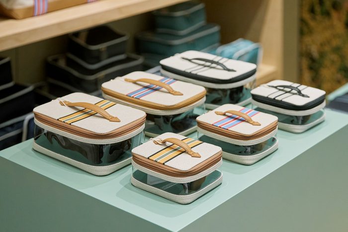 Clear-bottomed packing cases with striped canvas handles arranged on a mint display surface, with stacked blue packing cubes behind.