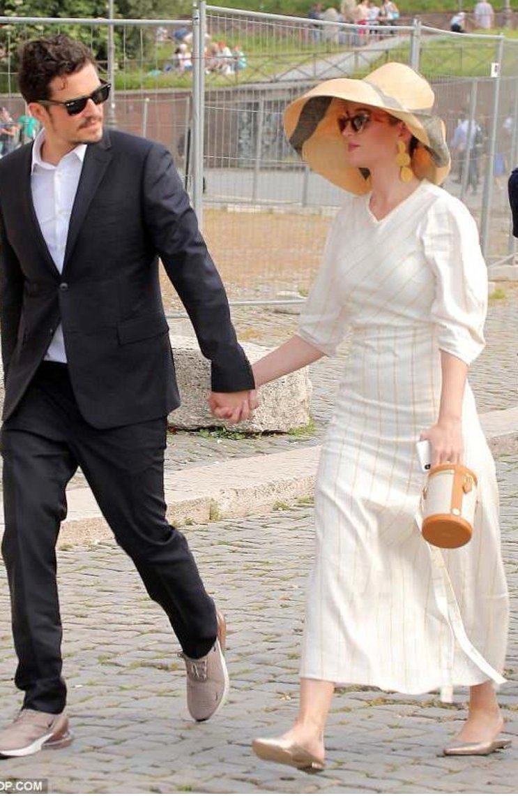 Katy Perry and Orlando Bloom walking hand in hand; Katy carries a Paravel cylinder bucket bag.