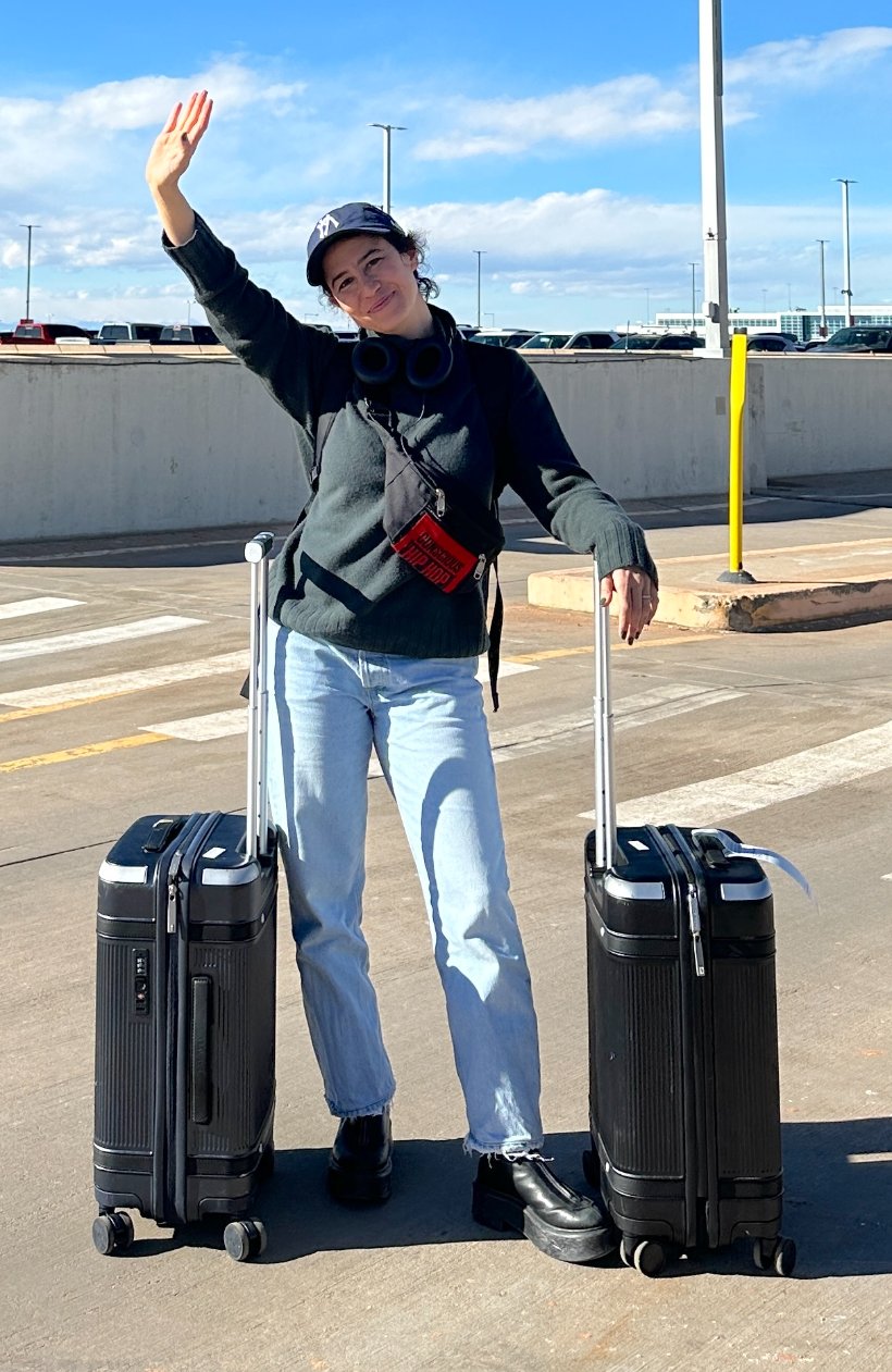 Ilana Glazer at airport curbside with two black Paravel Aviator carry-ons.