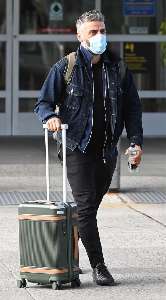 Oscar Isaac walking through the airport with an olive-green Paravel Aviator carry-on.