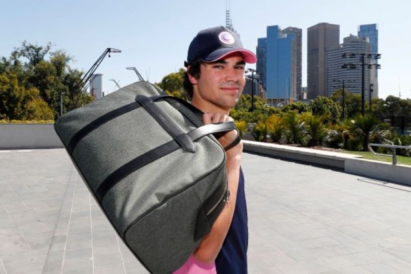 F1 driver Lance Stroll carrying an olive-green Paravel travel duffle over one shoulder.