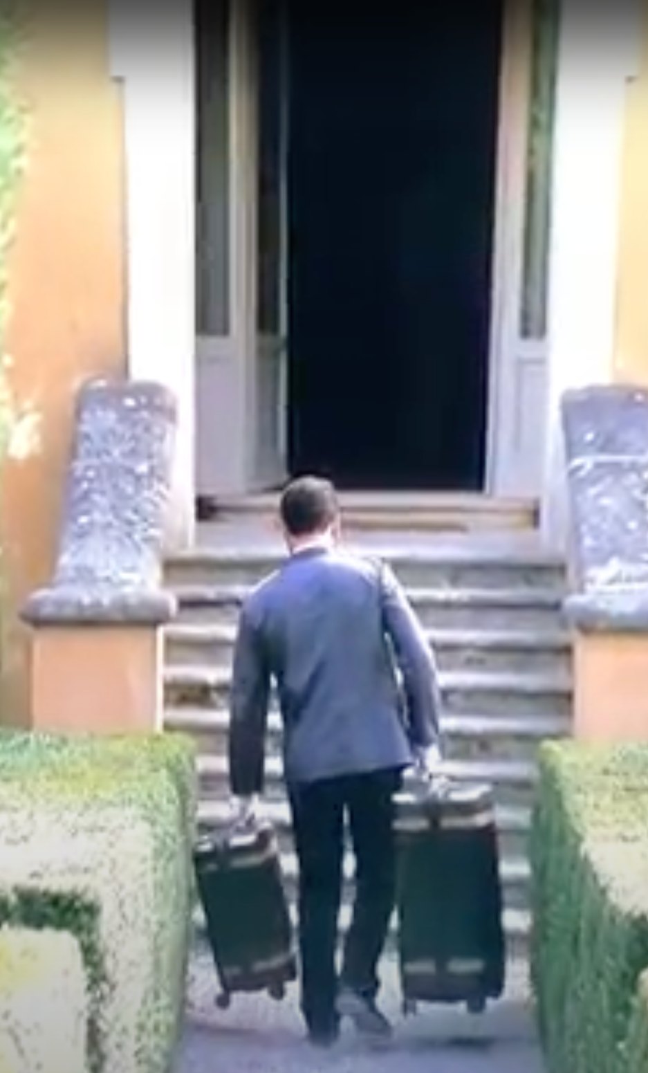 A still from Succession: a couple stands by a staircase with a Paravel carry-on between them.