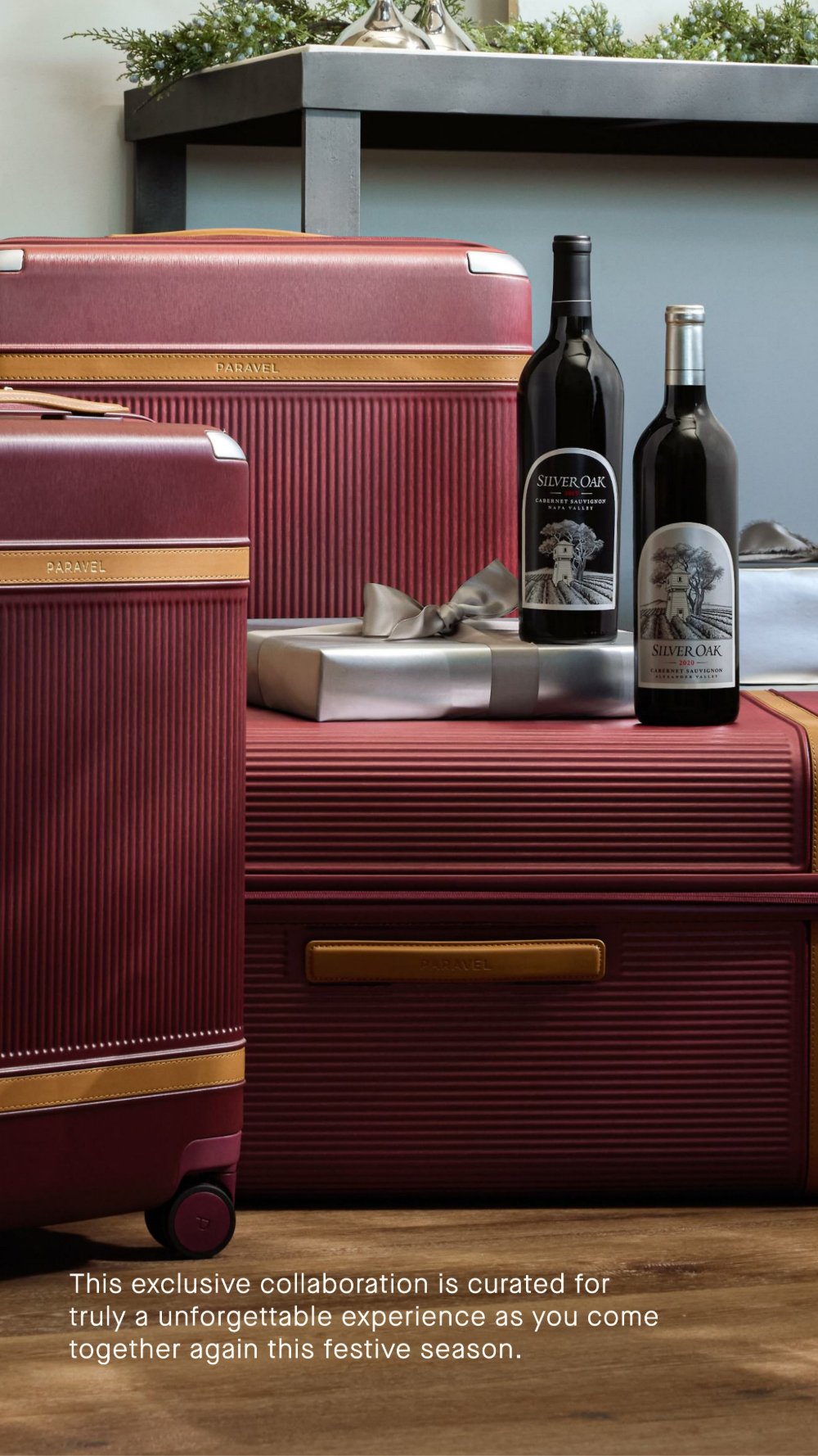 Styled oxblood Paravel trunk and carry-on with Silver Oak bottles and a silver-wrapped gift, set on a wood floor.