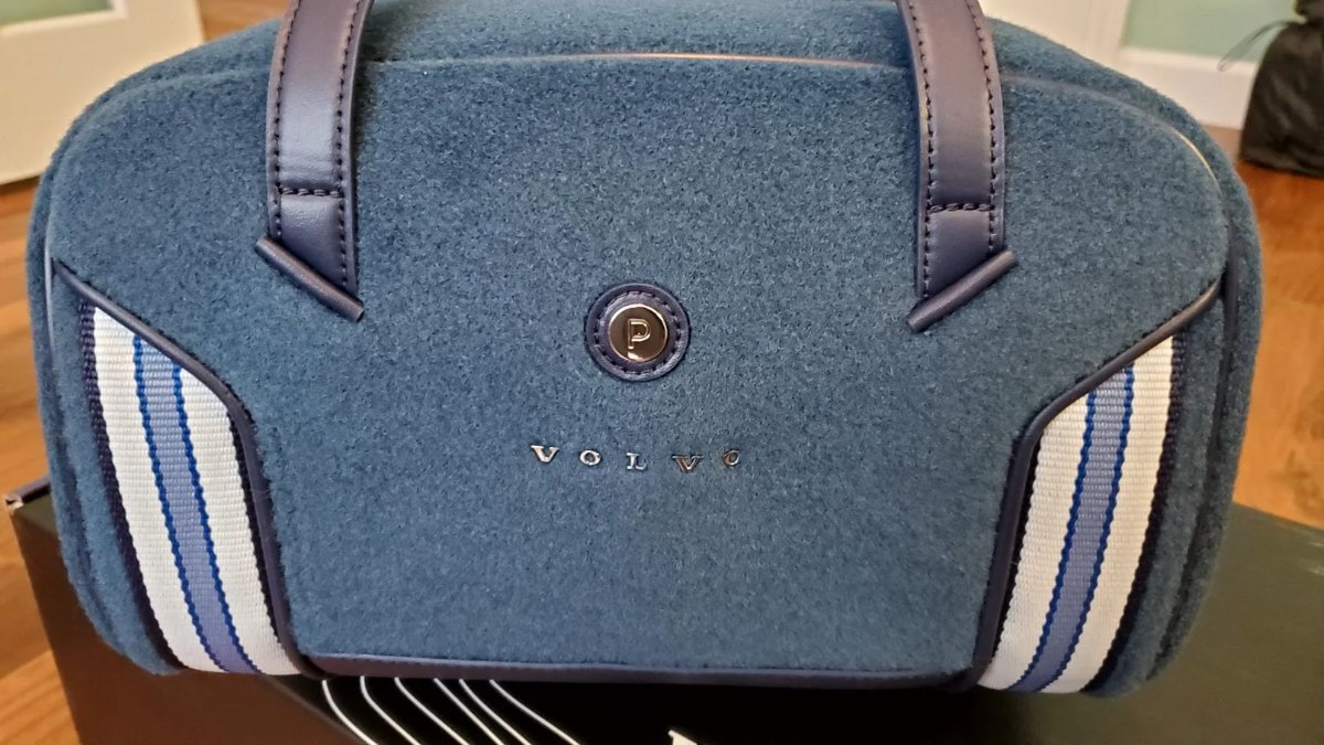A blue wool Paravel &lsquo;frunk&rsquo; bag with navy leather handles, a striped side panel, and a debossed VOLVO mark.