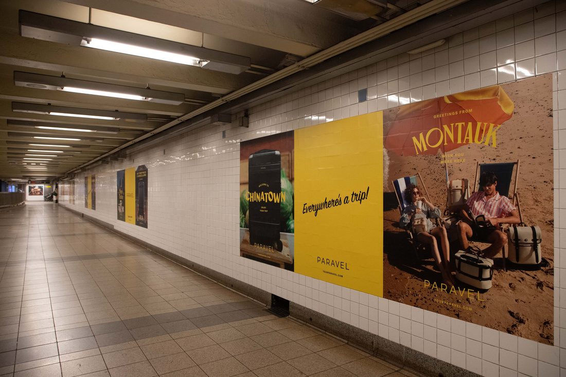 A tiled Broadway-Lafayette passage lined with PARAVEL posters — Chinatown, a yellow 'Everywhere's a trip!' panel, and a Montauk beach scene.