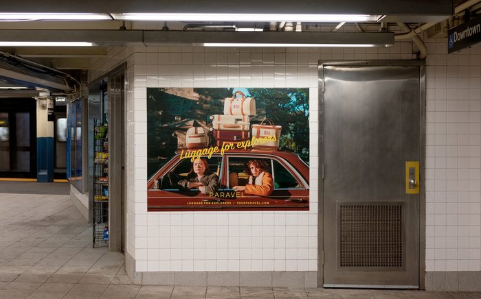 A large PARAVEL 'Luggage for explorers' poster on a tiled Broadway-Lafayette platform wall, a subway train across the tracks.