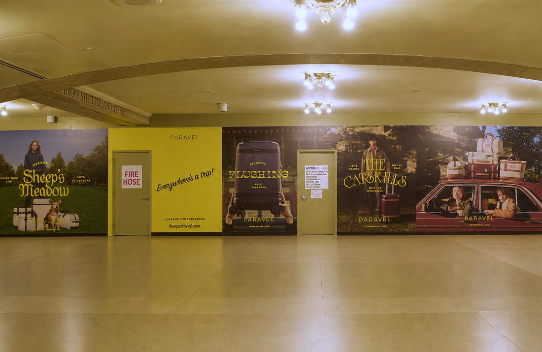 A long wall of PARAVEL posters under the vaulted Grand Central passage — Sheep's Meadow, Flushing, The Catskills — beside the Subway Shuttle sign.